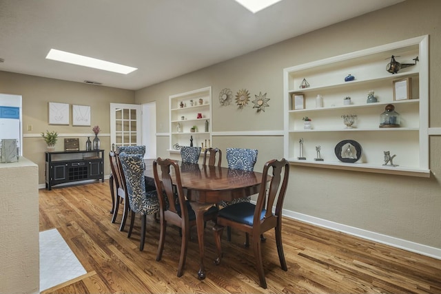 dining area featuring a skylight, built in shelves, baseboards, and wood finished floors