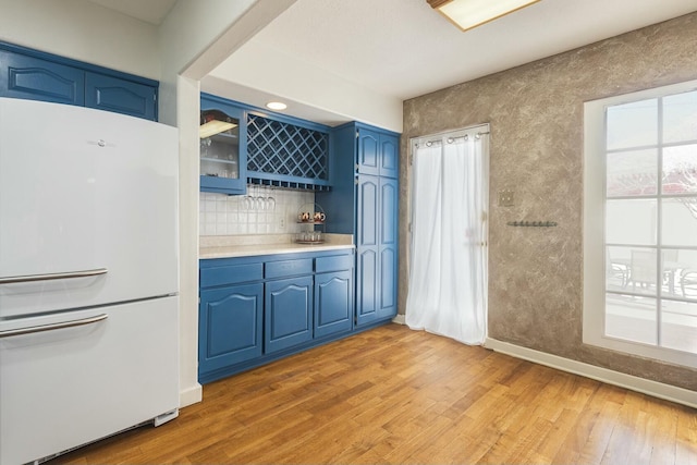 kitchen with light countertops, light wood-style flooring, decorative backsplash, freestanding refrigerator, and blue cabinets