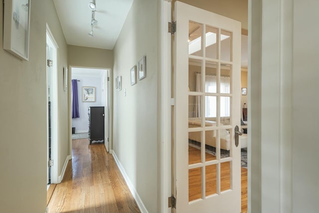 corridor featuring rail lighting, light wood-style flooring, baseboards, and french doors