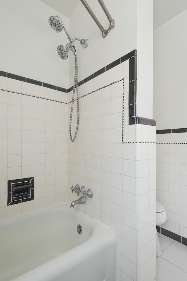 full bath featuring tile walls, bathing tub / shower combination, toilet, wainscoting, and tile patterned floors