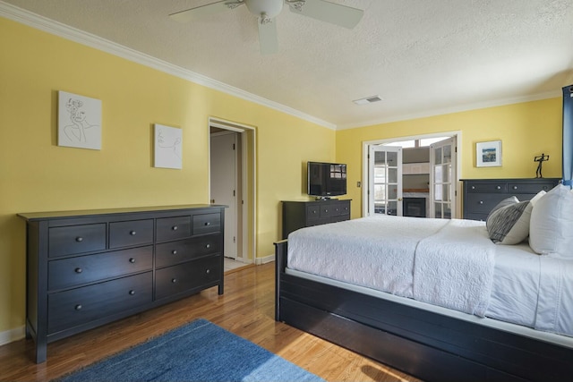 bedroom featuring visible vents, ornamental molding, a textured ceiling, wood finished floors, and baseboards