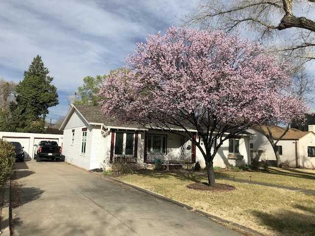 view of front facade with brick siding, a detached garage, roof with shingles, covered porch, and a front yard