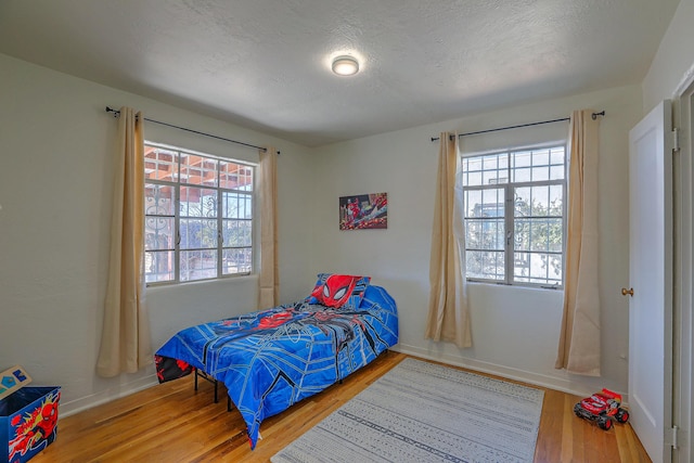 bedroom with a textured ceiling, baseboards, and wood finished floors