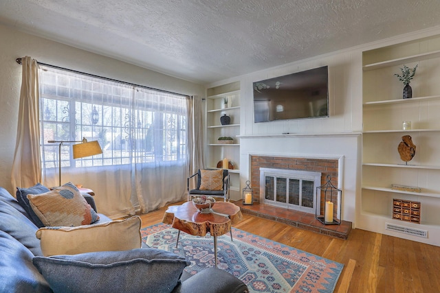 living room with a textured ceiling, a brick fireplace, wood finished floors, and built in features