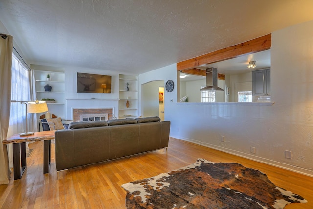 living room featuring baseboards, built in features, a textured ceiling, light wood-type flooring, and a fireplace