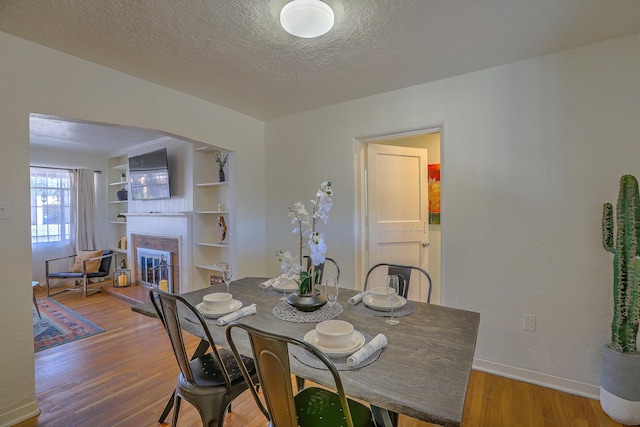 dining area with a textured ceiling, a glass covered fireplace, wood finished floors, and baseboards