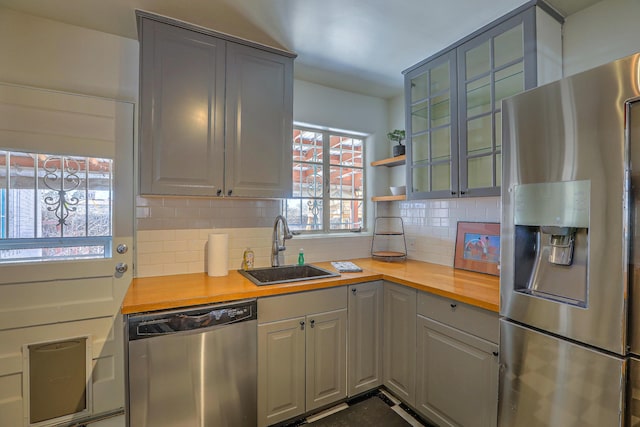 kitchen with stainless steel appliances, butcher block counters, decorative backsplash, glass insert cabinets, and a sink