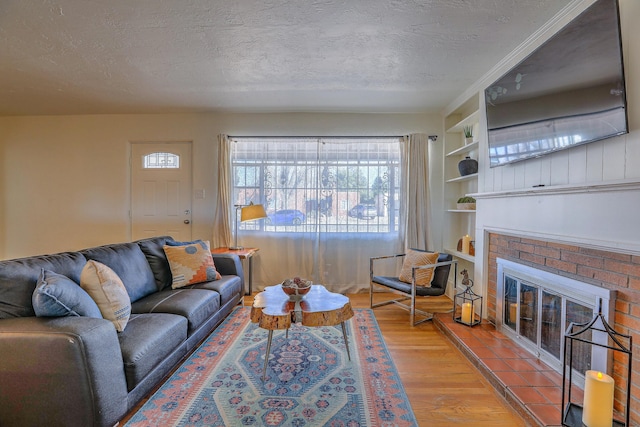 living room featuring built in shelves, a brick fireplace, a textured ceiling, and wood finished floors