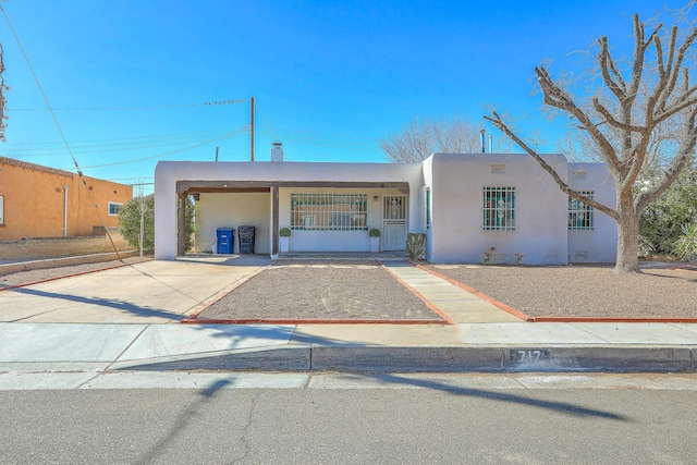 pueblo-style home with a carport, concrete driveway, and stucco siding