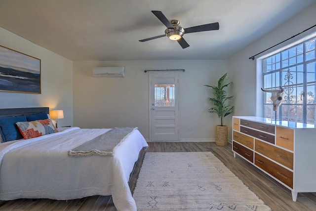 bedroom featuring ceiling fan, baseboards, an AC wall unit, and wood finished floors