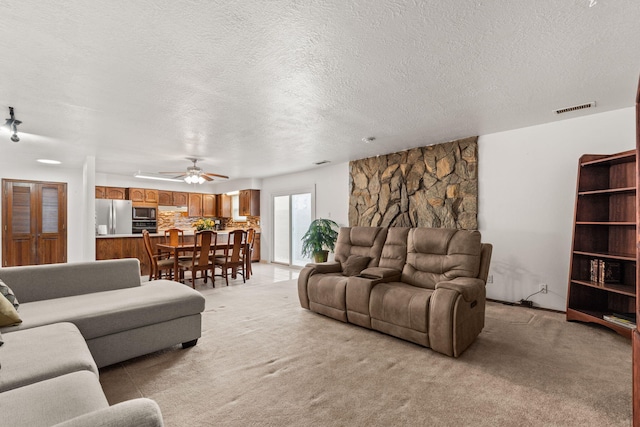 living room with a textured ceiling, ceiling fan, visible vents, and light colored carpet