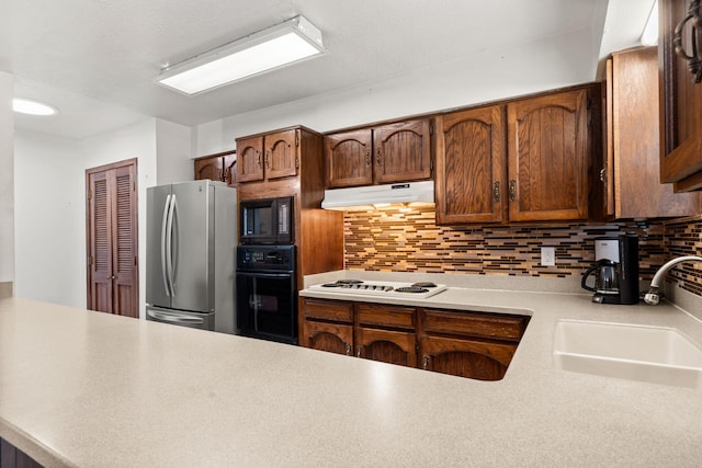 kitchen featuring black appliances, decorative backsplash, a sink, and under cabinet range hood