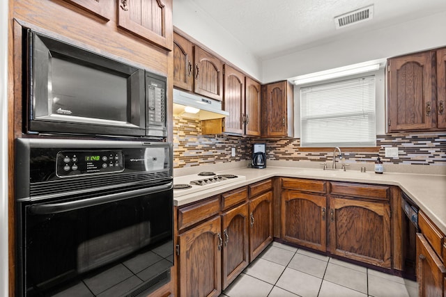 kitchen featuring light countertops, visible vents, a sink, under cabinet range hood, and black appliances