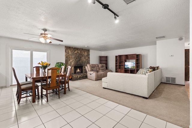 living room with a textured ceiling, a stone fireplace, visible vents, and light colored carpet