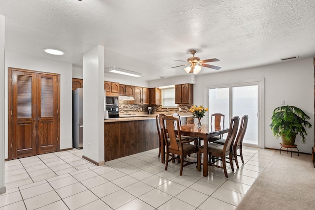 dining room with light tile patterned floors, visible vents, a ceiling fan, a textured ceiling, and baseboards