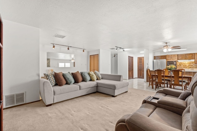 living area featuring light colored carpet, visible vents, ceiling fan, and a textured ceiling