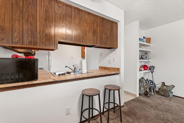 kitchen featuring light carpet, a kitchen breakfast bar, a textured ceiling, black microwave, and a sink