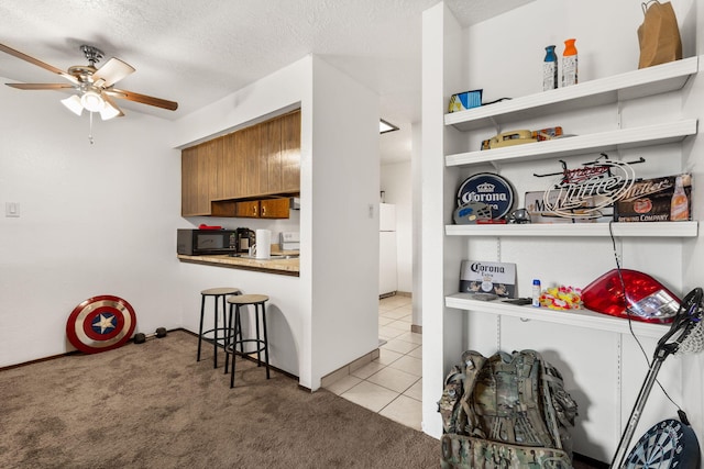 kitchen with black microwave, brown cabinetry, carpet flooring, and a textured ceiling