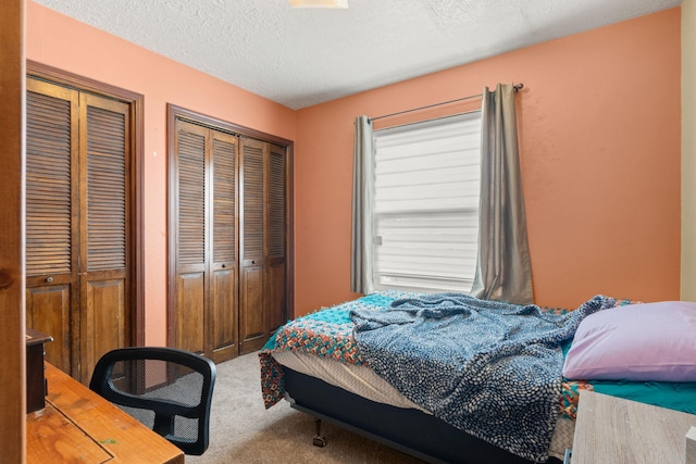 bedroom with a textured ceiling, carpet flooring, and two closets