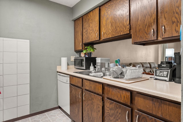 kitchen featuring light countertops, stainless steel microwave, white dishwasher, and a sink