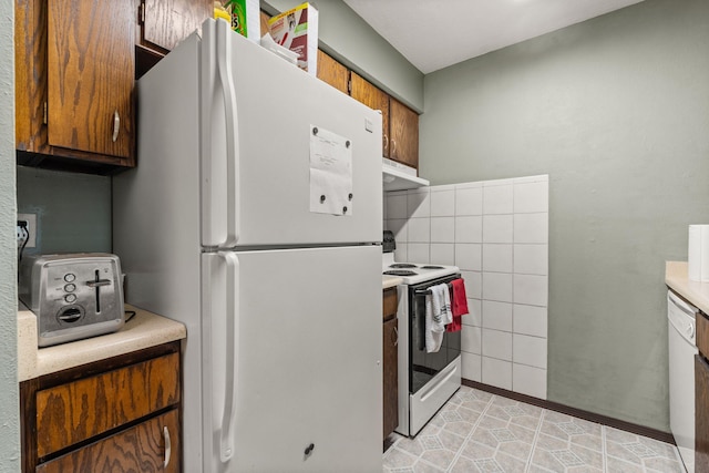 kitchen featuring white appliances, under cabinet range hood, light countertops, and brown cabinetry