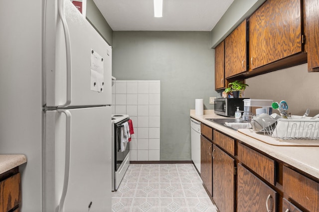 kitchen with light countertops, white appliances, brown cabinetry, and a sink