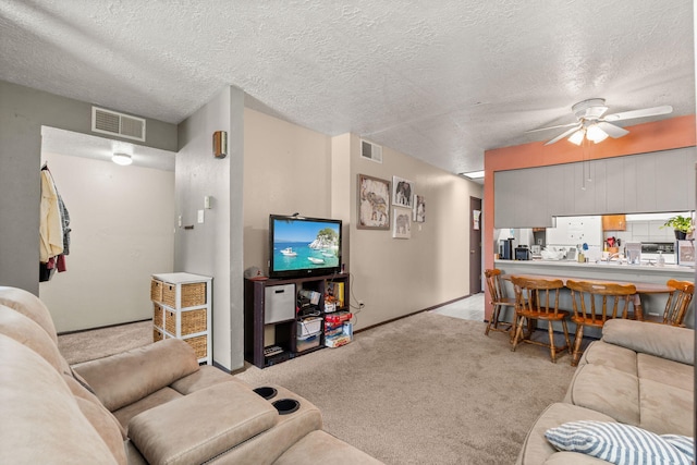 living area with light carpet, ceiling fan, visible vents, and a textured ceiling