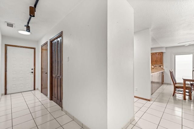 hall featuring light tile patterned floors, a textured ceiling, visible vents, baseboards, and track lighting