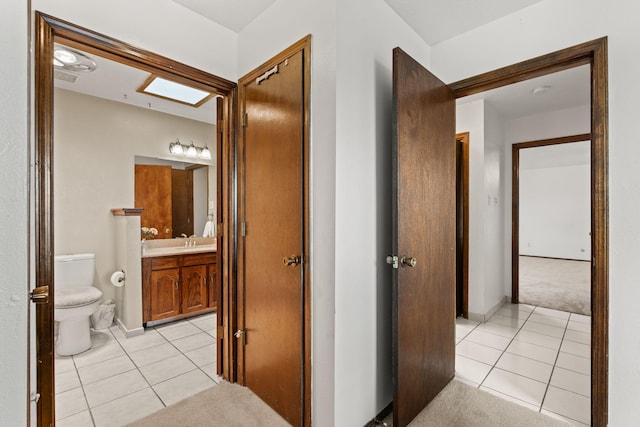 hallway with light carpet, a sink, baseboards, and light tile patterned floors