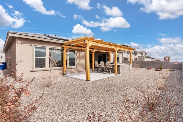 rear view of house with stucco siding, a pergola, roof mounted solar panels, a fenced backyard, and a patio area