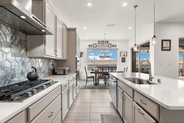 kitchen featuring light countertops, wall chimney range hood, stainless steel appliances, and a sink