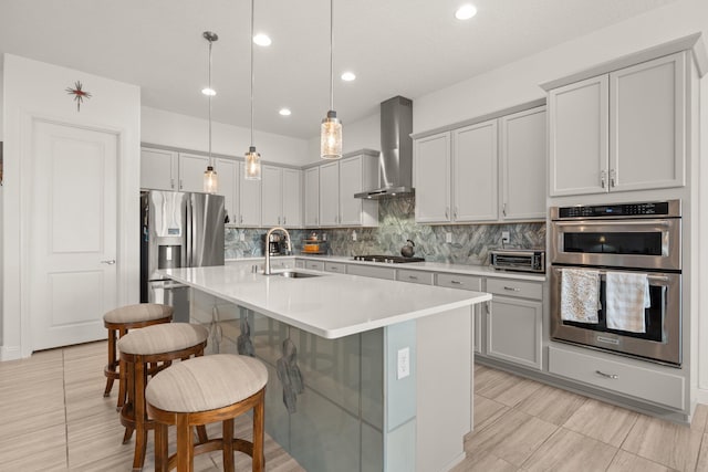 kitchen with a breakfast bar area, stainless steel appliances, decorative backsplash, a sink, and wall chimney range hood