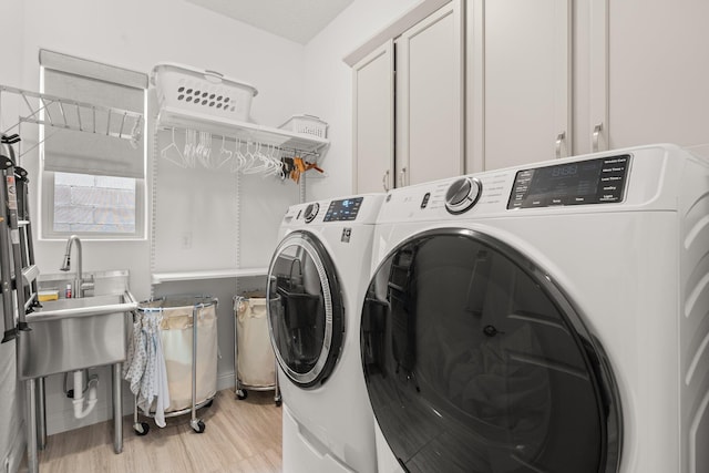 washroom featuring a sink, washing machine and dryer, cabinet space, and light wood-style flooring