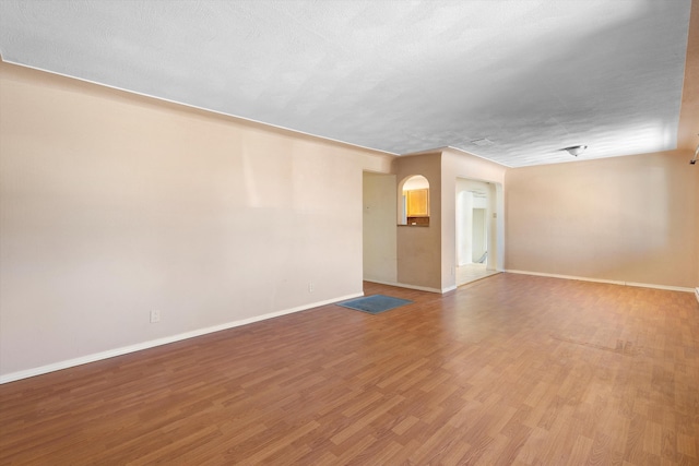 spare room featuring light wood-style floors, a textured ceiling, and baseboards