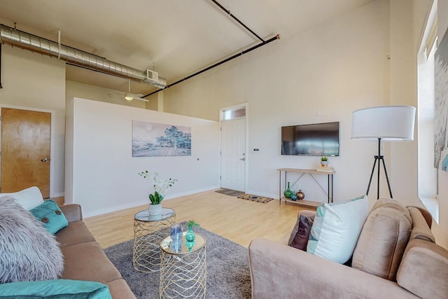 living room featuring a towering ceiling, baseboards, and wood finished floors