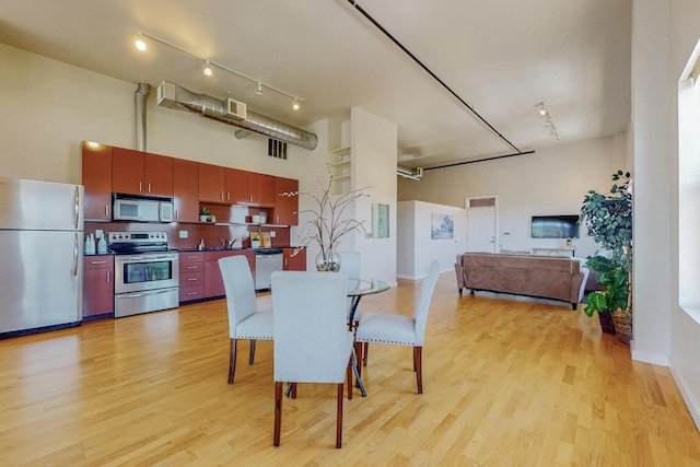 dining space with light wood finished floors, a high ceiling, visible vents, and rail lighting