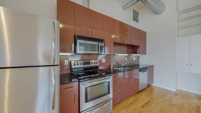 kitchen featuring visible vents, a towering ceiling, light wood-style flooring, appliances with stainless steel finishes, and a sink