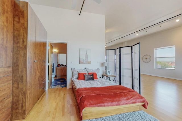 bedroom featuring baseboards, connected bathroom, light wood-style flooring, and track lighting