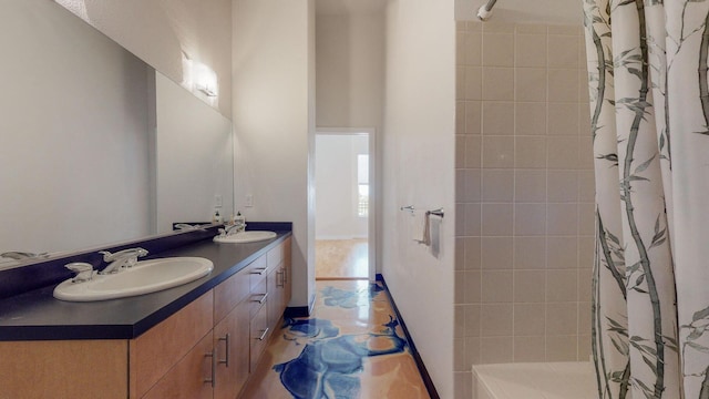 bathroom featuring tiled shower, a sink, and double vanity