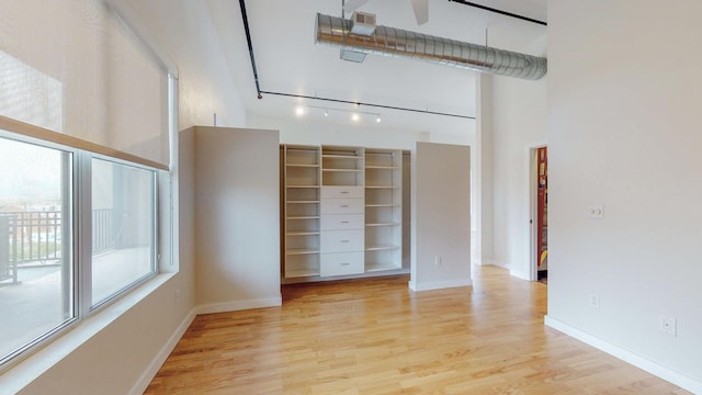 interior space with light wood finished floors, baseboards, a towering ceiling, ceiling fan, and rail lighting