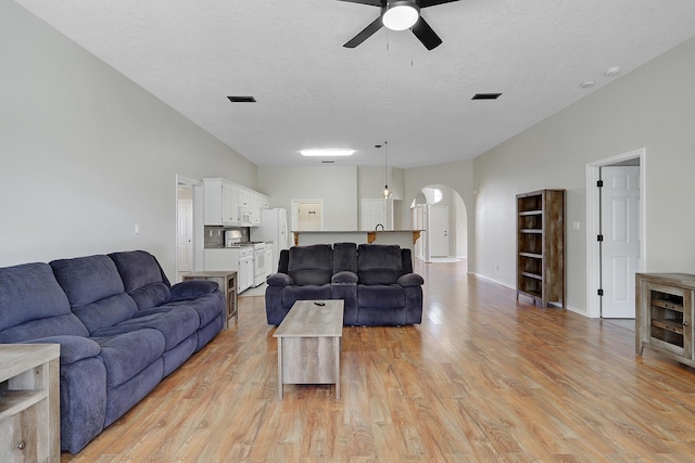 living room with light wood-type flooring, arched walkways, visible vents, and a textured ceiling