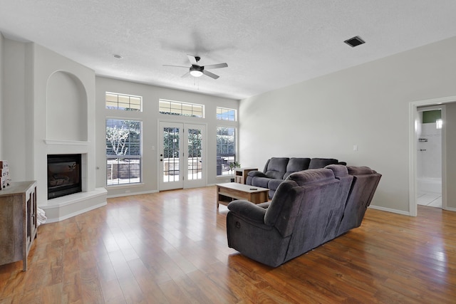 living room with baseboards, a ceiling fan, a glass covered fireplace, wood finished floors, and a textured ceiling