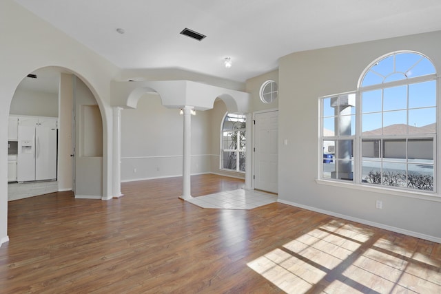 spare room featuring baseboards, visible vents, ornate columns, and wood finished floors