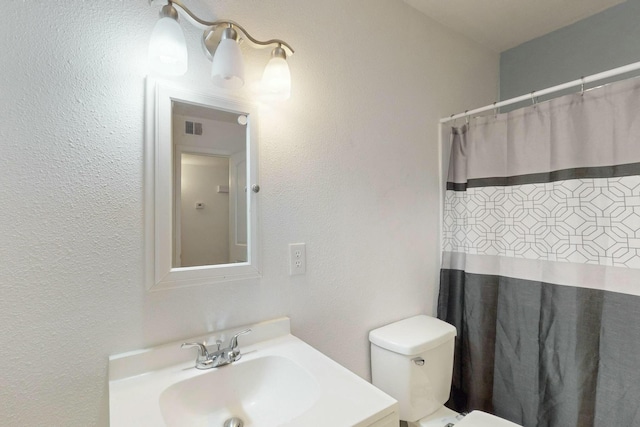 full bath with visible vents, toilet, a shower with curtain, a textured wall, and vanity