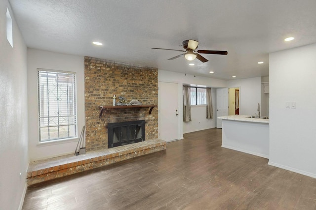 unfurnished living room featuring a brick fireplace, baseboards, wood finished floors, a textured ceiling, and a ceiling fan