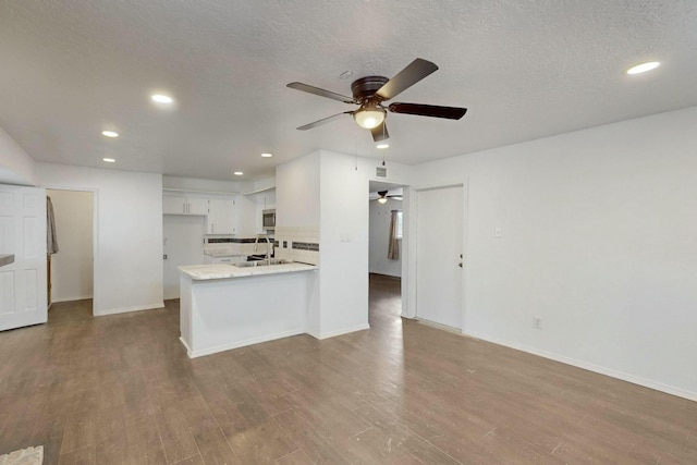 kitchen featuring a ceiling fan, a sink, stainless steel microwave, backsplash, and wood finished floors