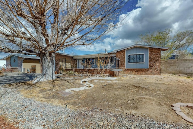 view of front of home with an attached carport, brick siding, and fence