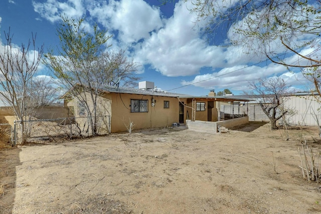 rear view of property with stucco siding, a chimney, and fence