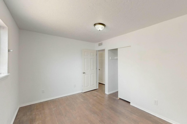 spare room with a textured ceiling, wood finished floors, visible vents, and baseboards