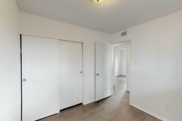 unfurnished bedroom featuring visible vents, baseboards, wood finished floors, a closet, and a textured ceiling